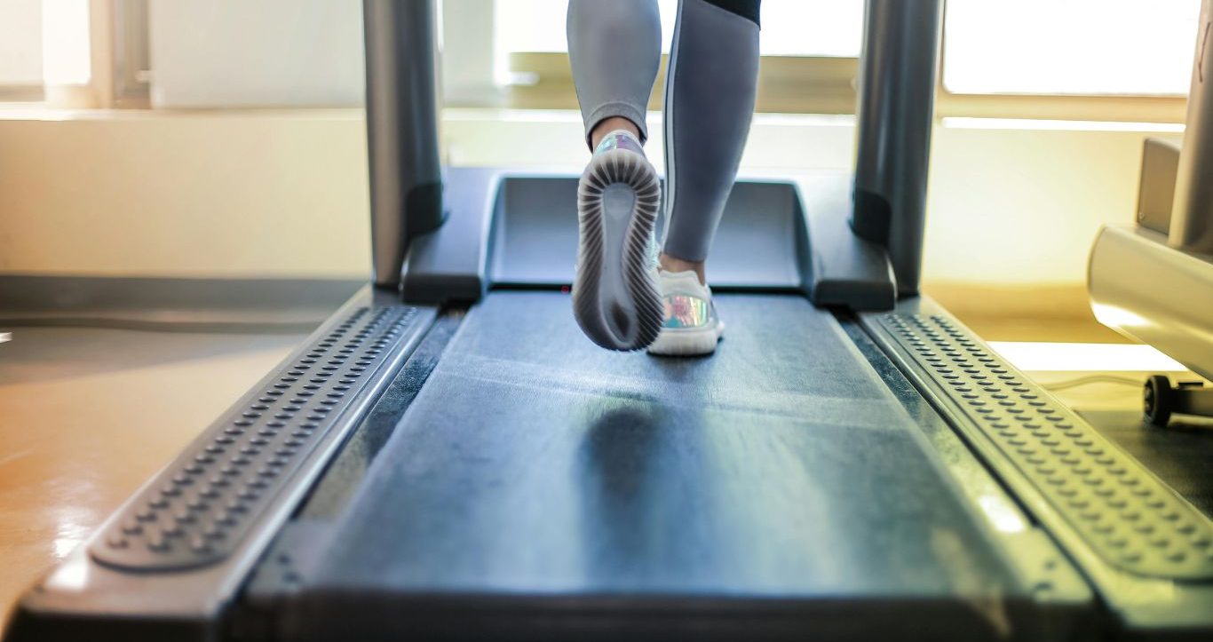 Des pieds de femme dans des baskets qui marchent sur un tapis de course 