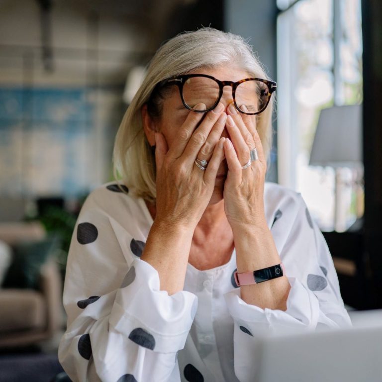 Une femme aux cheveux blancs et lunettes qui met ses mains sur ses yeux