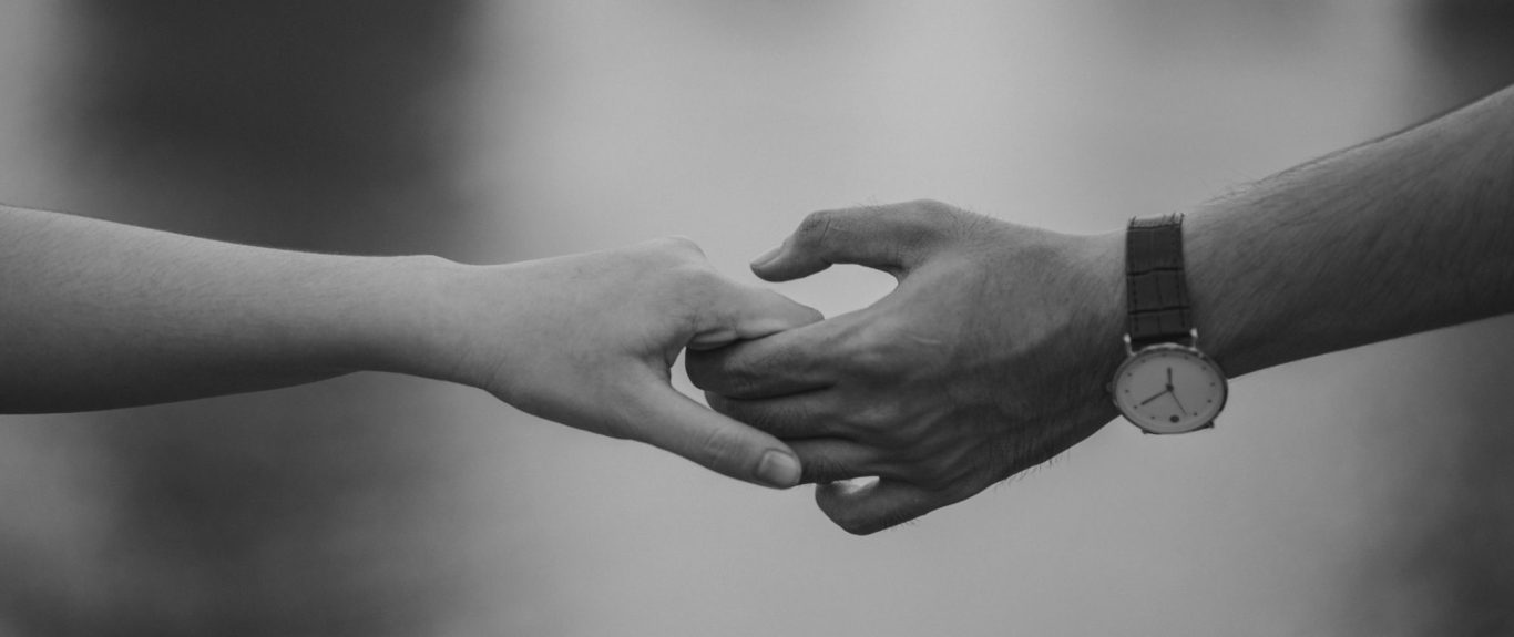 Une main de femme et une main d'homme qui se tiennent du bout des doigts, en noir et blanc